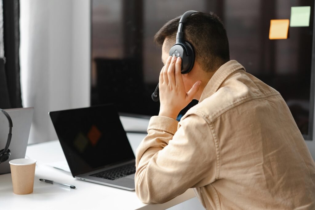 pexels photo 7681302 7681302 A man wearing headphones works at a laptop in a modern office setting.